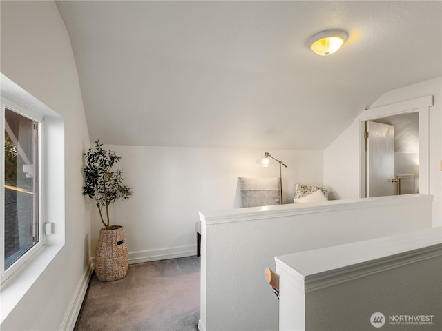 corridor featuring baseboards, carpet flooring, and vaulted ceiling