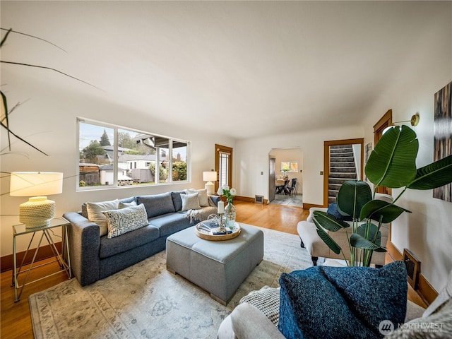 living room featuring arched walkways, stairs, baseboards, and wood finished floors