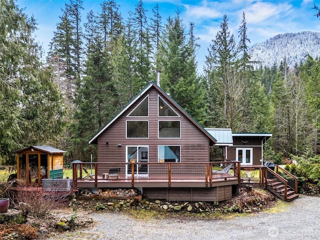 rear view of house with french doors, a wooden deck, and a wooded view