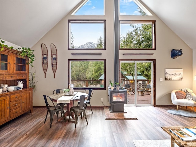 dining area featuring baseboards, high vaulted ceiling, wood finished floors, and a wood stove