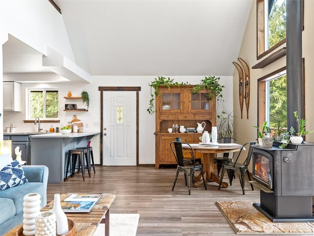 dining space featuring high vaulted ceiling, a wood stove, and light wood finished floors