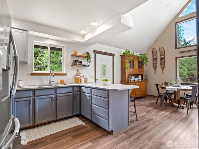 kitchen with gray cabinetry, a breakfast bar, stainless steel refrigerator with ice dispenser, a sink, and a peninsula