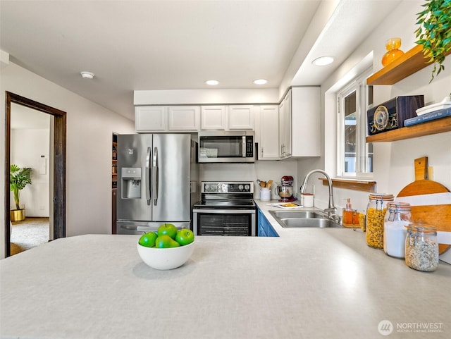 kitchen with a sink, light countertops, white cabinets, stainless steel appliances, and open shelves