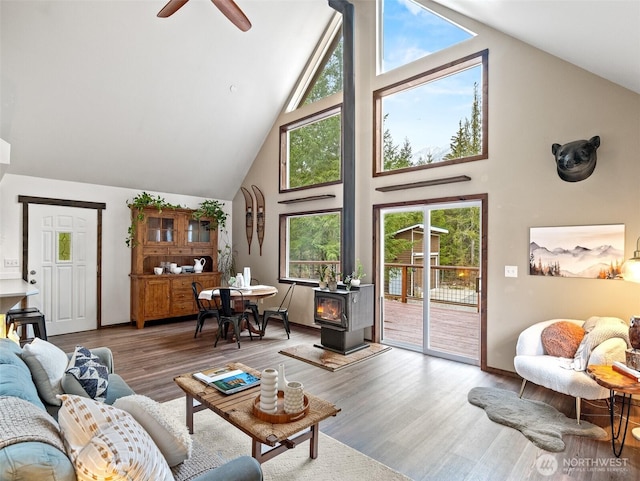 living room featuring a wood stove, wood finished floors, high vaulted ceiling, and ceiling fan