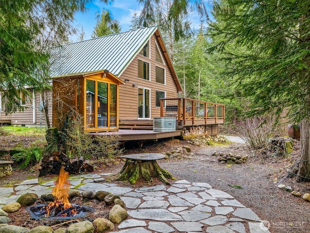 rear view of property with metal roof, a deck, a standing seam roof, and an outdoor fire pit