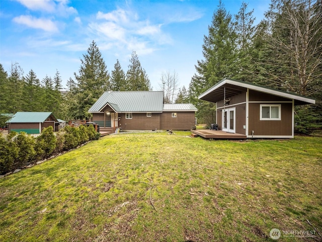 back of property with a wooden deck, an outbuilding, a yard, and metal roof