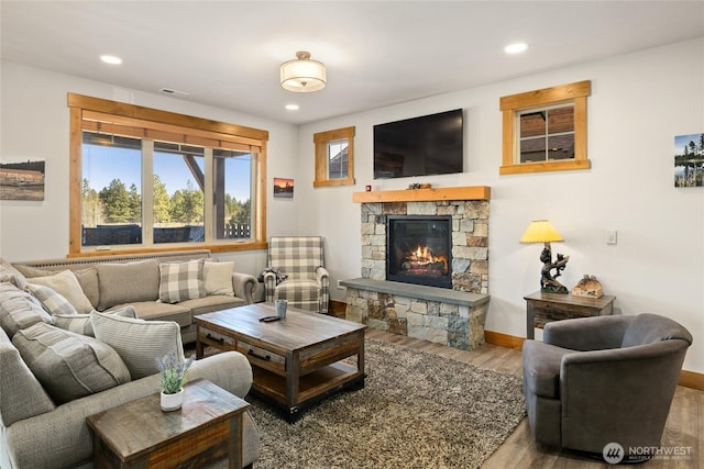 living area featuring baseboards, visible vents, wood finished floors, a stone fireplace, and recessed lighting