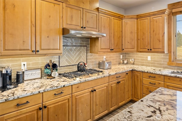 kitchen featuring under cabinet range hood, tasteful backsplash, stainless steel gas stovetop, and light stone counters