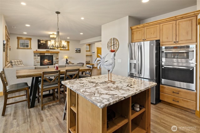 kitchen featuring stainless steel appliances, open floor plan, light brown cabinetry, open shelves, and light wood finished floors