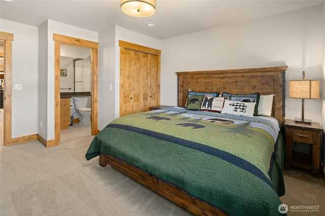 carpeted bedroom with a closet, ensuite bath, and baseboards