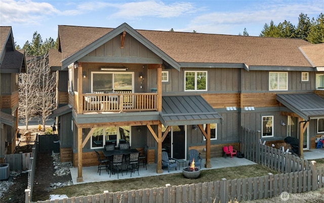 rear view of house with a fenced backyard, a fire pit, roof with shingles, board and batten siding, and a patio area