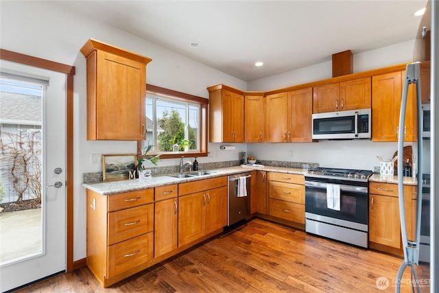 kitchen featuring light stone counters, wood finished floors, stainless steel appliances, and a sink