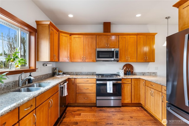 kitchen with a sink, light stone counters, dark wood-style floors, and stainless steel appliances