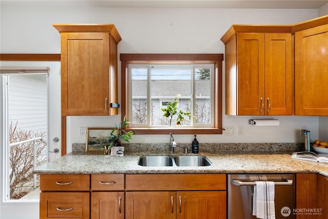 kitchen with stainless steel dishwasher, light stone countertops, brown cabinets, and a sink