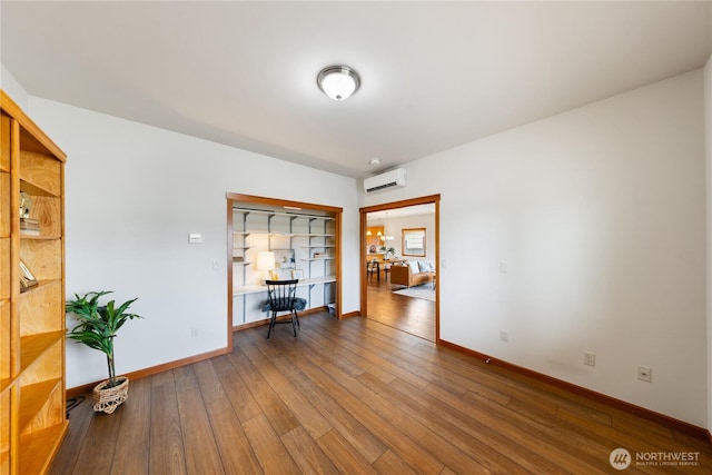 unfurnished room featuring baseboards, a wall unit AC, and hardwood / wood-style flooring