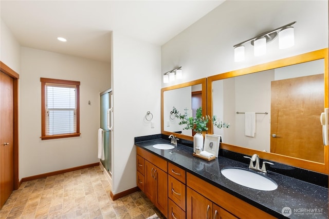 full bathroom featuring double vanity, a shower stall, baseboards, and a sink