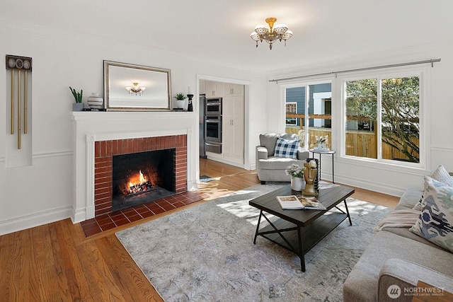 living room featuring crown molding, a brick fireplace, wood finished floors, and baseboards