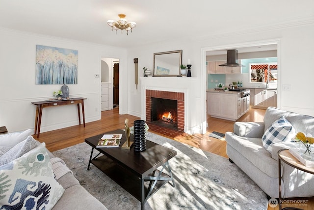 living room with arched walkways, light wood finished floors, a fireplace, and ornamental molding