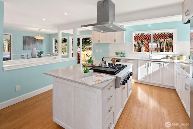 kitchen with backsplash, a center island, light wood-style flooring, island exhaust hood, and stainless steel gas stovetop