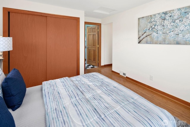 bedroom featuring visible vents, wood finished floors, a closet, baseboards, and attic access