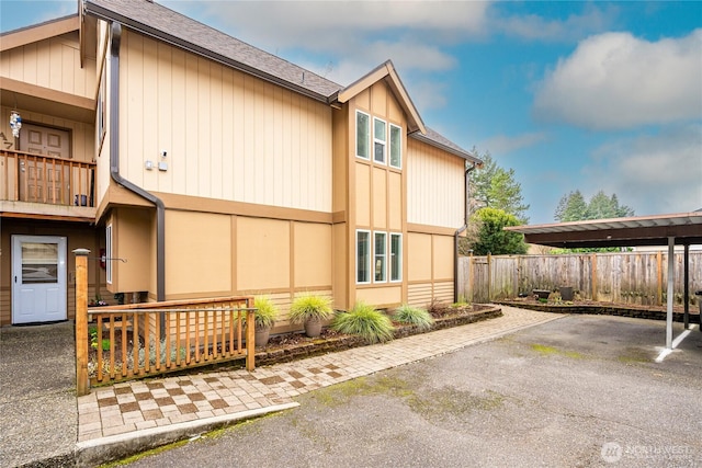 view of home's exterior with covered parking, a balcony, roof with shingles, and fence