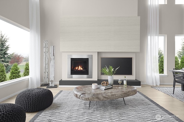 living room featuring a glass covered fireplace, light wood-style floors, baseboards, and a towering ceiling