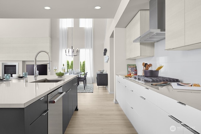 kitchen with wall chimney range hood, light countertops, an inviting chandelier, stainless steel appliances, and a sink