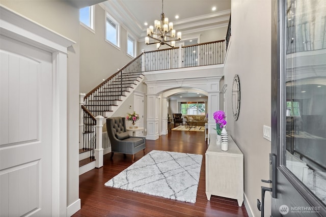 foyer featuring a notable chandelier, ornamental molding, hardwood / wood-style floors, arched walkways, and stairs