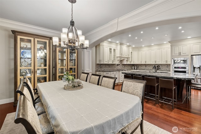 dining space with a notable chandelier, ornamental molding, recessed lighting, arched walkways, and dark wood-style flooring