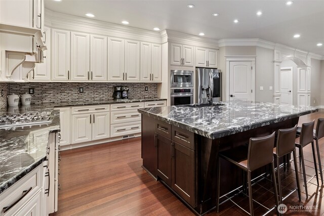 kitchen featuring dark wood finished floors, dark brown cabinetry, appliances with stainless steel finishes, a breakfast bar area, and white cabinets