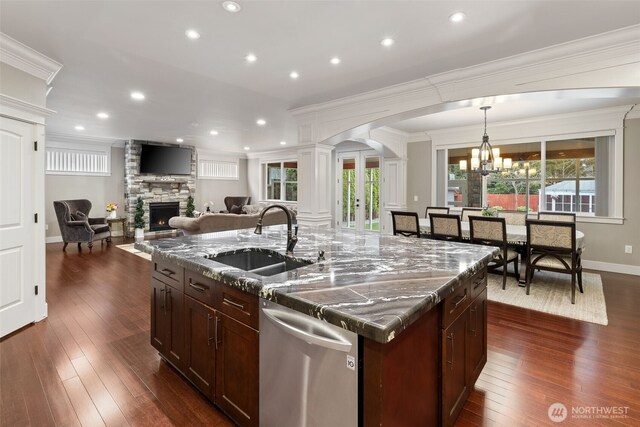 kitchen with a stone fireplace, french doors, stainless steel dishwasher, arched walkways, and a sink