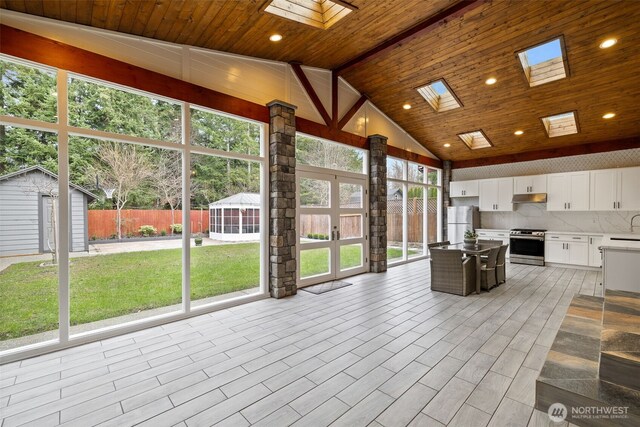 unfurnished sunroom featuring vaulted ceiling with skylight and wood ceiling