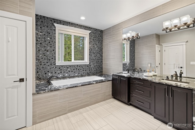 bathroom with a bath, double vanity, tile walls, and a sink