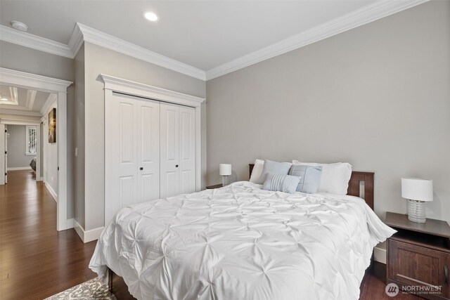 bedroom featuring a closet, baseboards, dark wood-type flooring, and crown molding