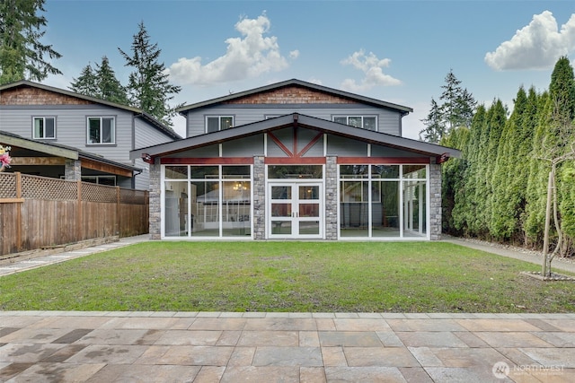 rear view of house featuring stone siding, a lawn, and a sunroom