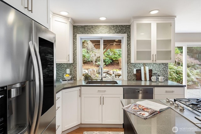 kitchen with a sink, stainless steel appliances, glass insert cabinets, white cabinetry, and tasteful backsplash