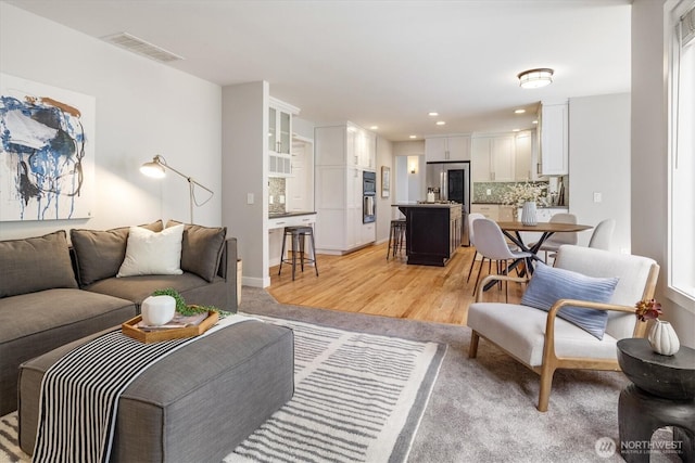 living room featuring baseboards, recessed lighting, visible vents, and light wood-type flooring