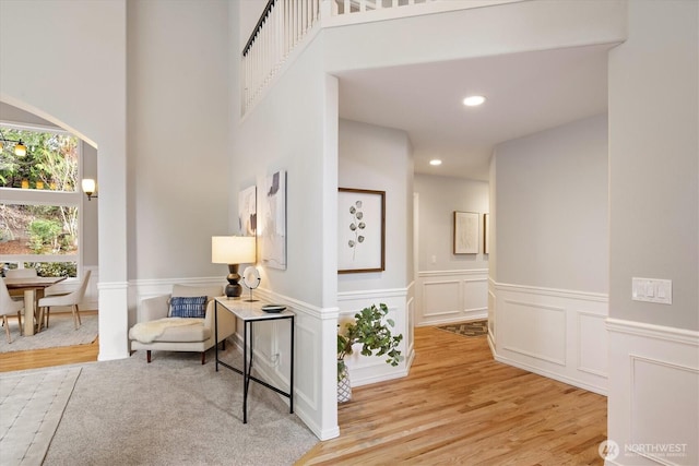 hallway with wainscoting, recessed lighting, a towering ceiling, wood finished floors, and a decorative wall