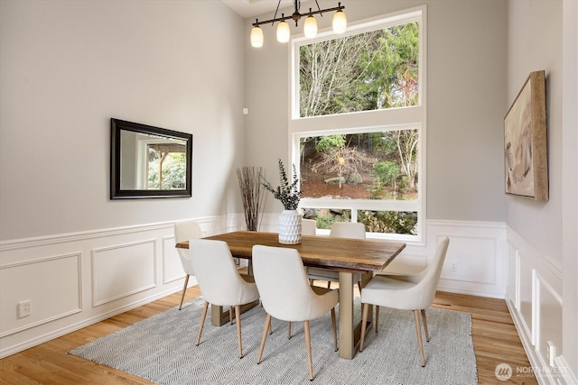 dining room with light wood-type flooring, an inviting chandelier, wainscoting, and a decorative wall