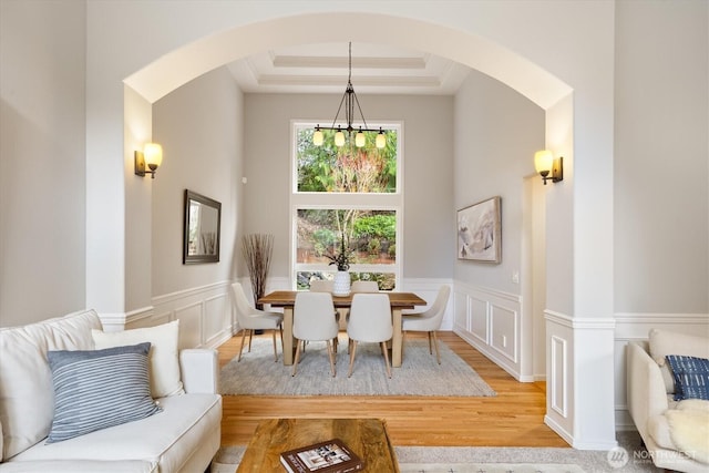 dining area featuring wood finished floors, arched walkways, wainscoting, a decorative wall, and a raised ceiling