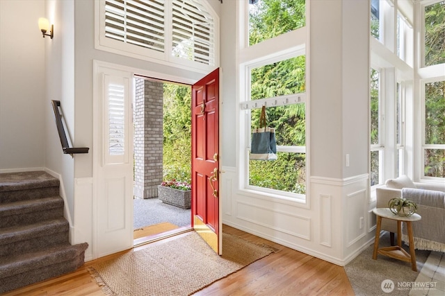 entrance foyer with stairway, a towering ceiling, a wainscoted wall, and wood finished floors