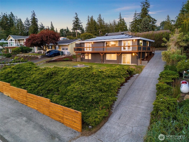 view of front of property featuring a front lawn, roof mounted solar panels, and a wooden deck