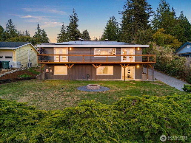 back of property at dusk featuring a wooden deck, roof mounted solar panels, a lawn, and an outdoor fire pit