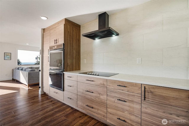 kitchen featuring dark wood-style floors, stainless steel double oven, light countertops, and wall chimney range hood