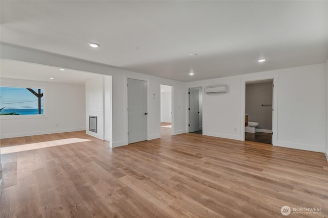 interior space with a wall mounted air conditioner, light wood-style flooring, baseboards, and a glass covered fireplace