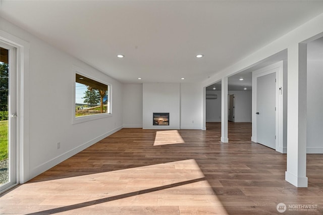 unfurnished living room featuring a glass covered fireplace, recessed lighting, baseboards, and wood finished floors