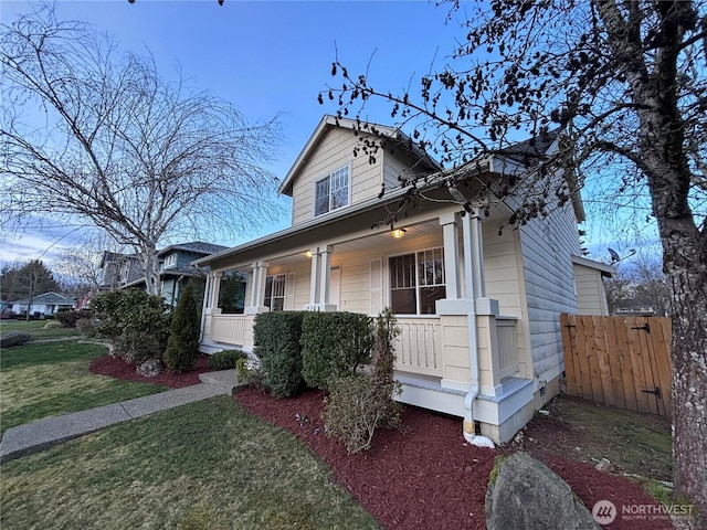 view of front facade with covered porch, a front yard, and fence