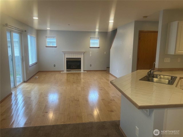 unfurnished living room with recessed lighting, a tile fireplace, light wood-style floors, and a sink