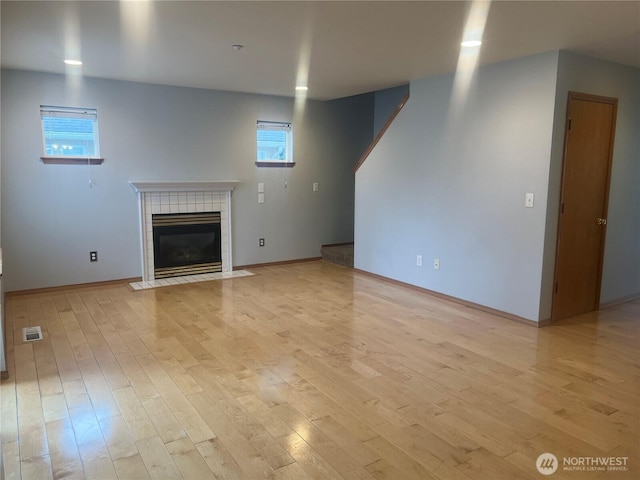 unfurnished living room with light wood-type flooring, baseboards, visible vents, and a tiled fireplace