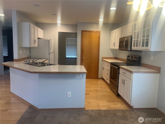 kitchen featuring a sink, stainless steel appliances, a peninsula, white cabinets, and glass insert cabinets